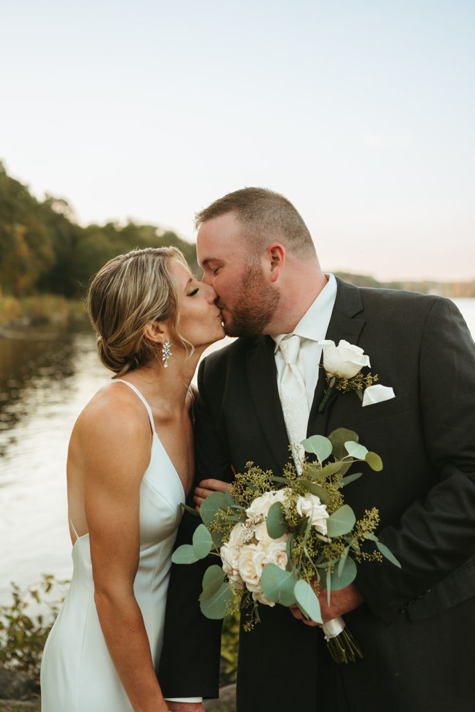 bride and groom kissing near water